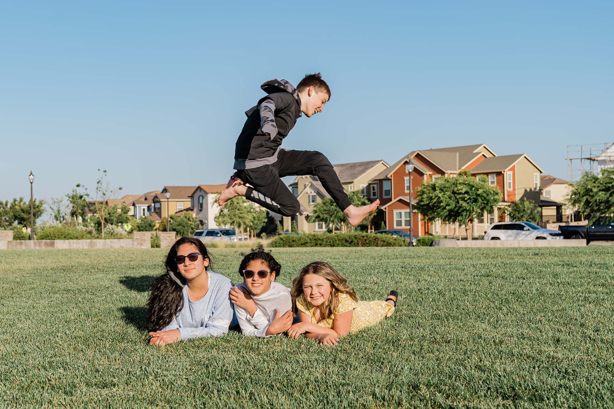 Boy jumping over three girls in a park.